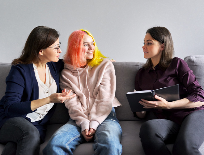 Mother, teen, and therapist sitting together on a couch during a supportive family therapy session, discussing mental health and strengthening communication.