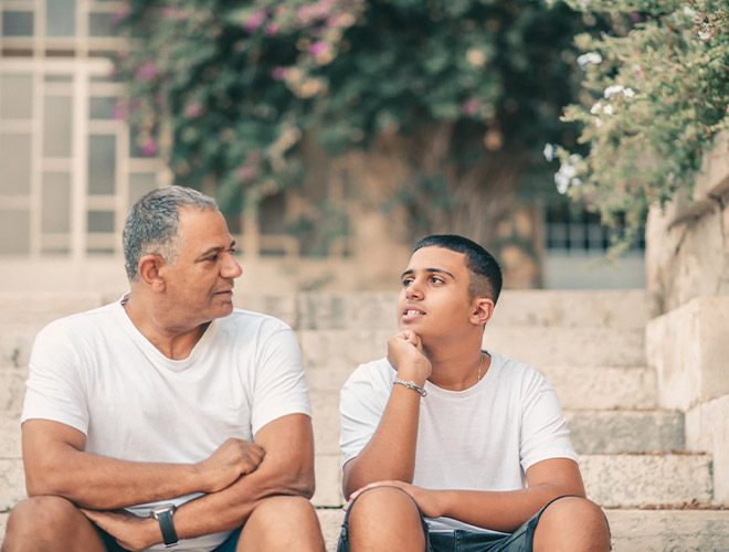 A father and teen son sitting together on outdoor steps having a calm, connected conversation