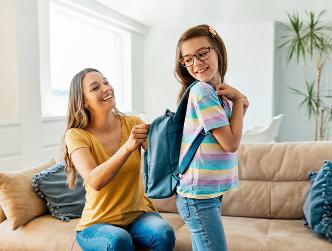 A parent helping her daughter get her backpack ready for the new school year